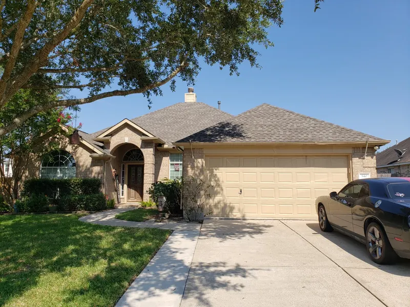 Front view of a brick home with a newly shingled gray roof and a large tree